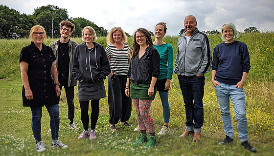 Ein Teambild mit 8 Personen auf einer grünen Wiese. Das Bild wurde auf dem Gelände der Jugendbildungsstätte LidiceHaus aufgenommen.